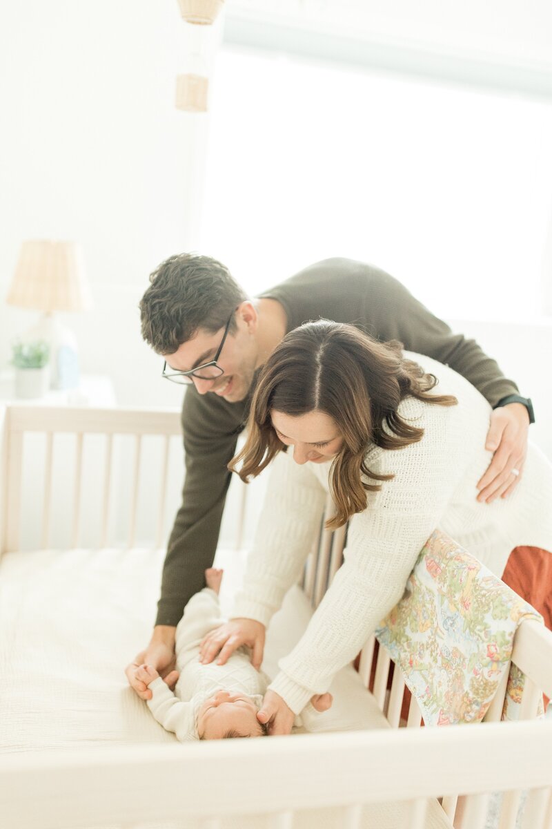 a mom and dad leaning over a crib putting a baby to sleep