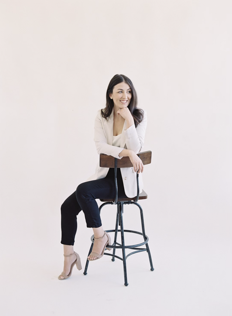 Sarah Wahhab, owner of Mulberry & Moss Floral Design headshot brunette on a stool.