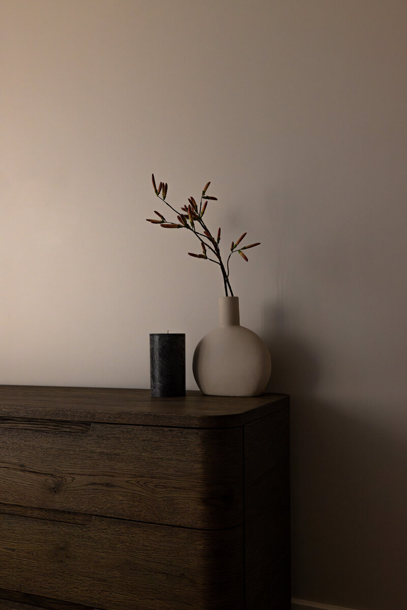 Close-up of a dark wood dresser styled with a candle, book, and faux florals in a bedroom of the luxury Park City condo, designed by Sister Studio.