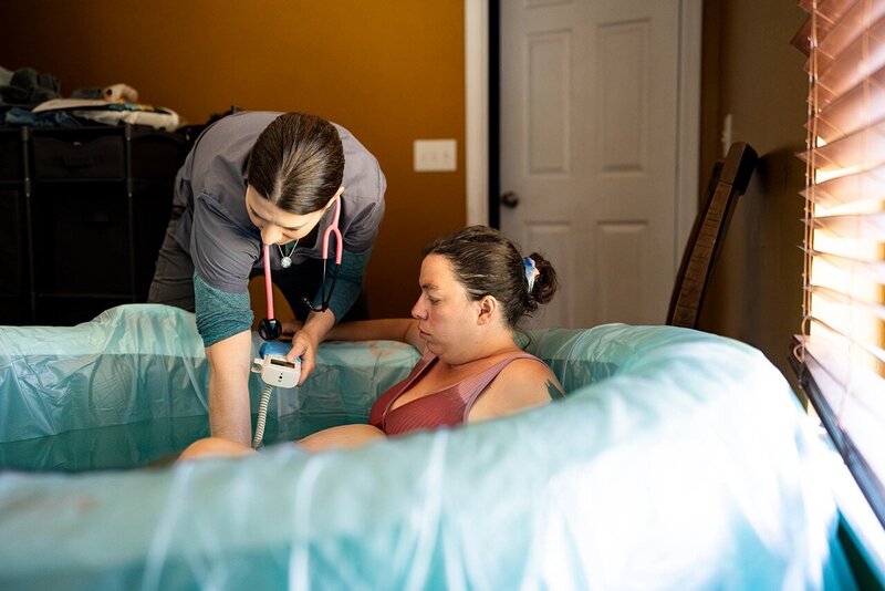 Woman laboring in birthing pool while the midwife listens for baby's heartbeat at a homebirth photo session in the Lowcountry