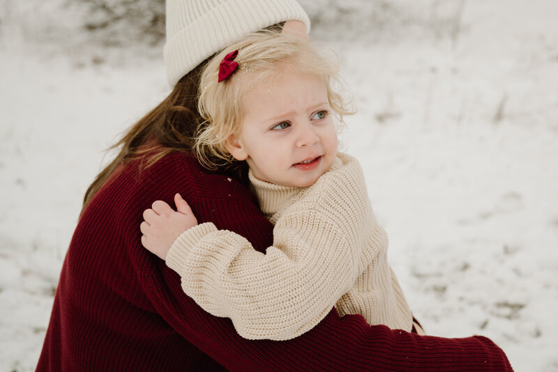 Mama hugging her daughter  in the snow while daughter is looking back.