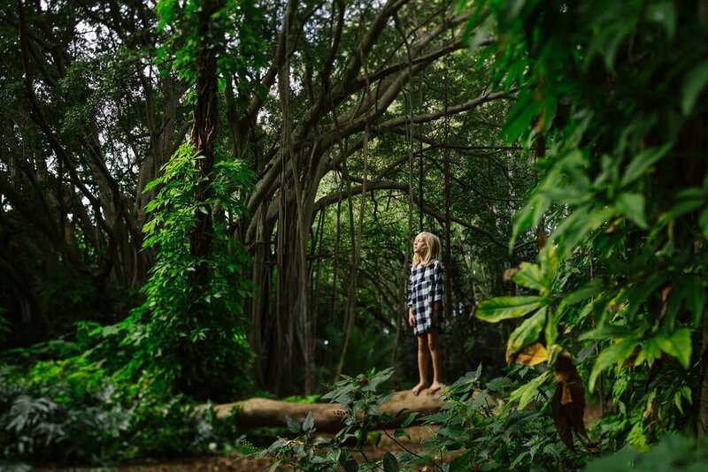 A little girl is standing on a wood branch in a tropical jungle.