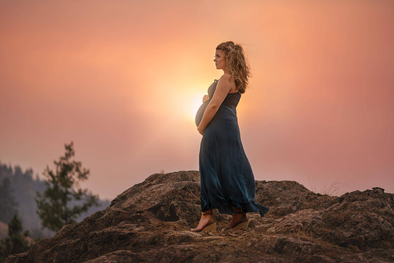 A beautiful pregnant woman standing against a dramatic sunset in Kamloops.
