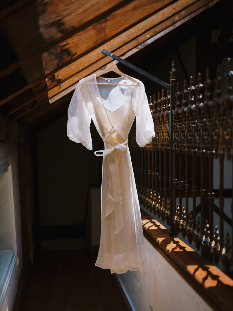 white wedding dress hangs from rafters in moody rustic venue