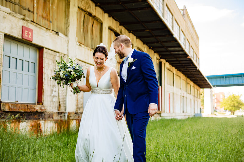 Wedding couple laughing and holding hands while walking through a field in the Glass city metropark in Toledo Ohio