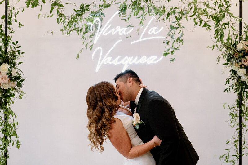 bride and groom kissing under neon sign