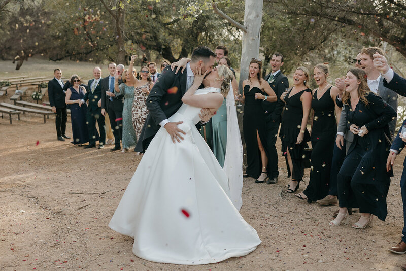 Bride and groom kissing while their guests throw flower pedals in New Braunfels Texas.