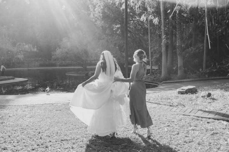A bride walks toward a lake at Brisbane Botanical Gardens as she prepares for her wedding portraits