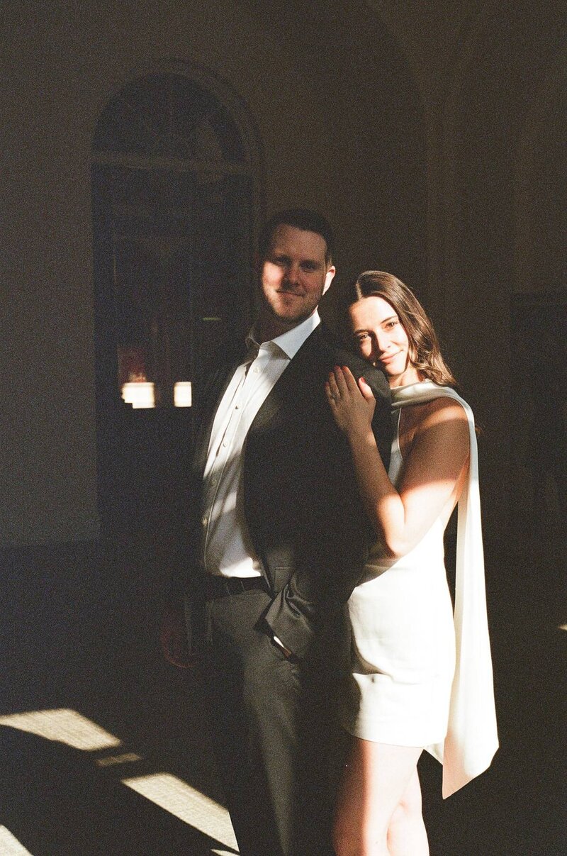 A couple stands by the window as the woman embraces her partner from behind captured on 35mm film