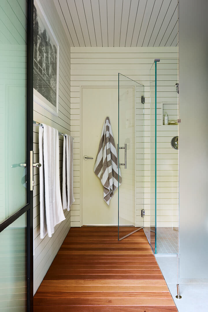 Interior designers in Boston design a Hingham pool house bathroom with teak flooring, shiplap walls, and a sleek modern coastal style.