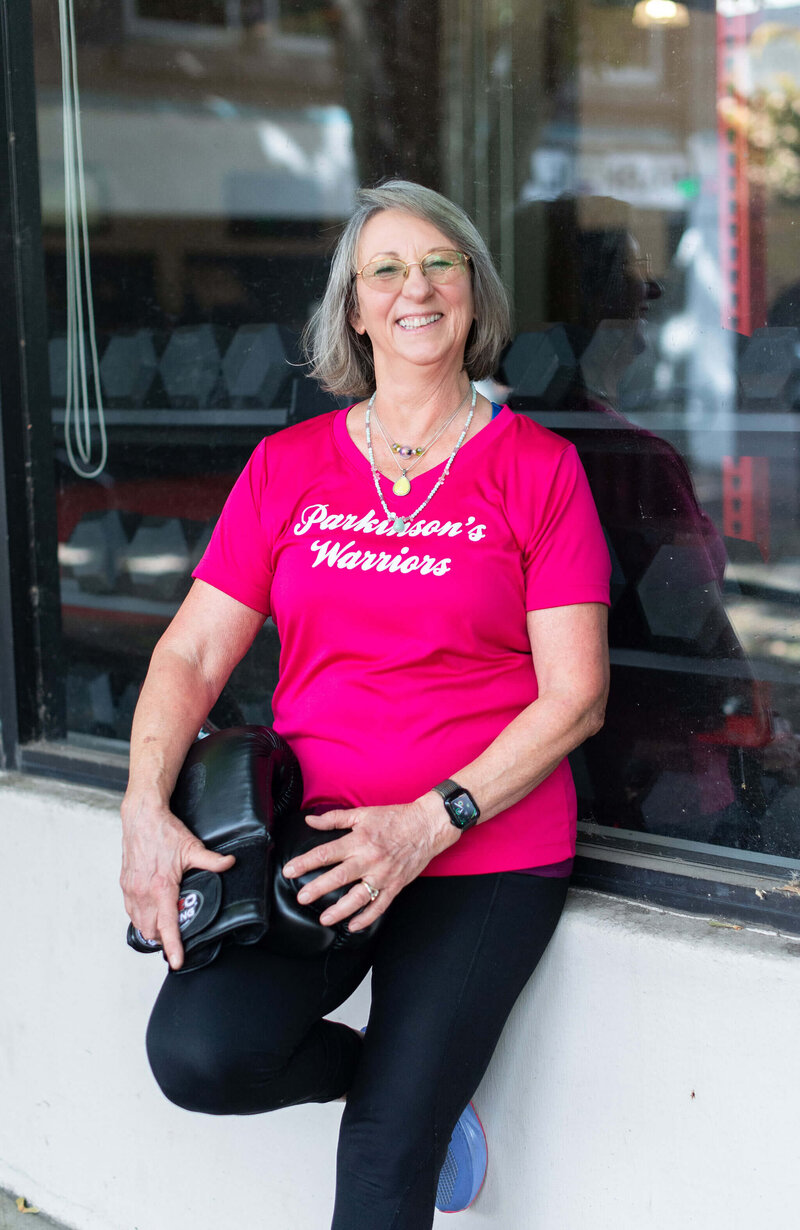 Coach Lori of the Oregon Parkinson's Warriors Foundation smiles and holds boxing gloves. 