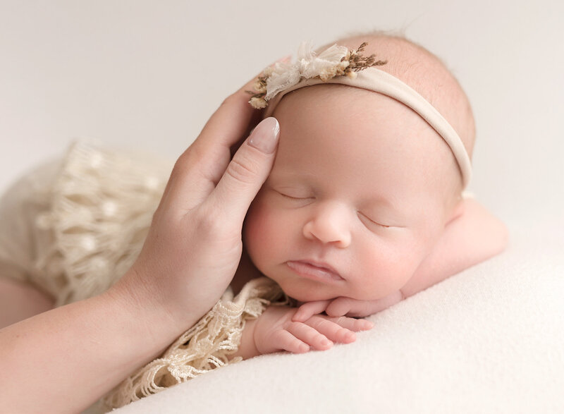 baby girl on cream backdrop with mom hand caressing her face