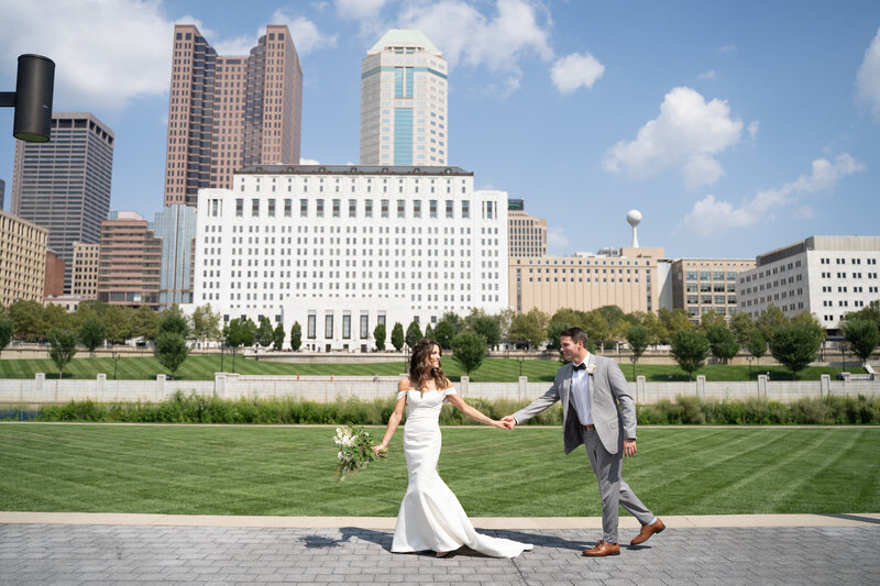 Bride, Alexis, leads her groom, Tyler, as they walk in front of the beautiful Columbus, Ohio skyline.