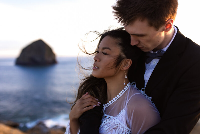 Groom holding his bride close with the Oregon coastline in the background, photographed by an Oregon Coast Elopement and Wedding Photographer.