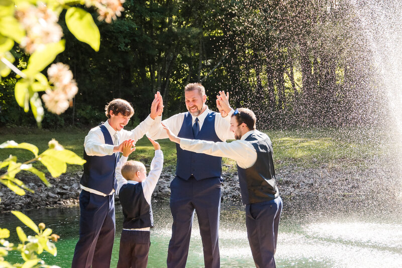 Groomsmen standing on a dock, with a fountain flowing in the background, high-fiving in a circle.