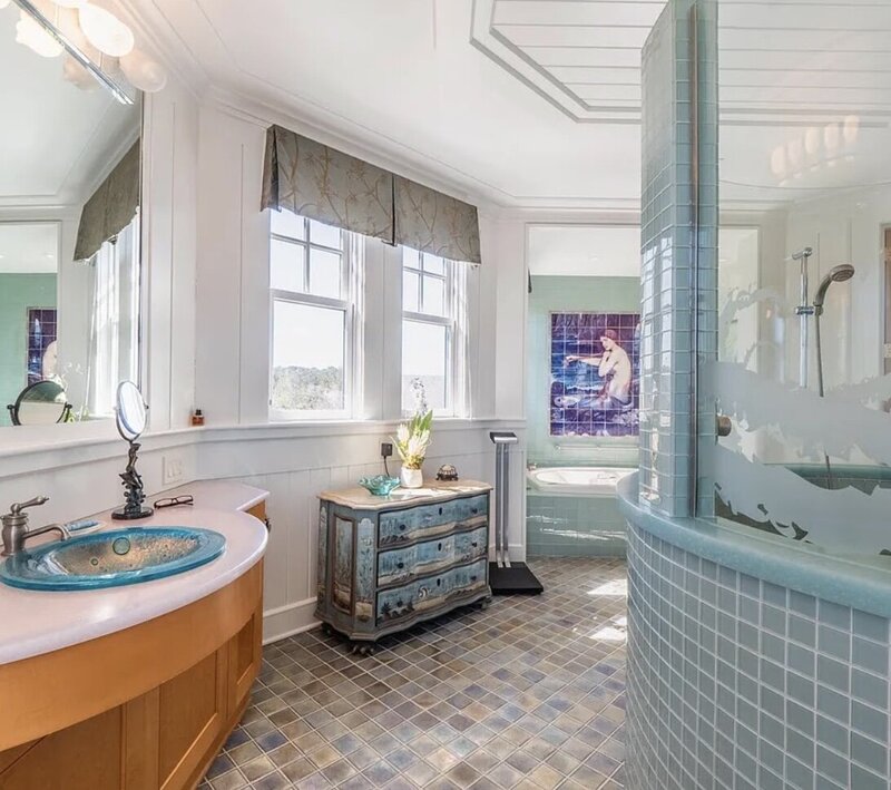 Serene coastal bathroom from The Carolina project by Dwelling Place Interiors, featuring soft neutral tones, elegant tilework, a spa-like soaking tub, and natural light. A perfect blend of warmth and sophistication for a tranquil retreat.
