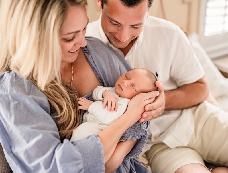 Mother and father smiling down at their newborn baby during an in-home newborn session