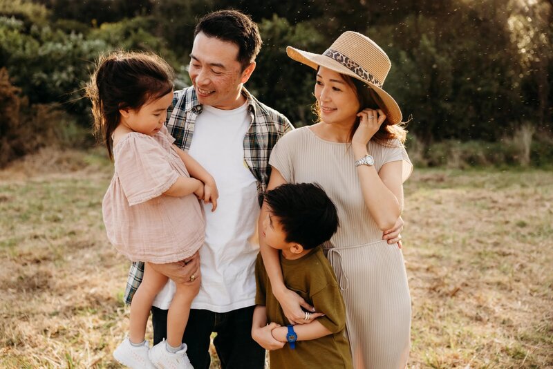 a family with two children hugging and laughing during a photoshoot with auckland photographer michelle kelly at an auckland park
