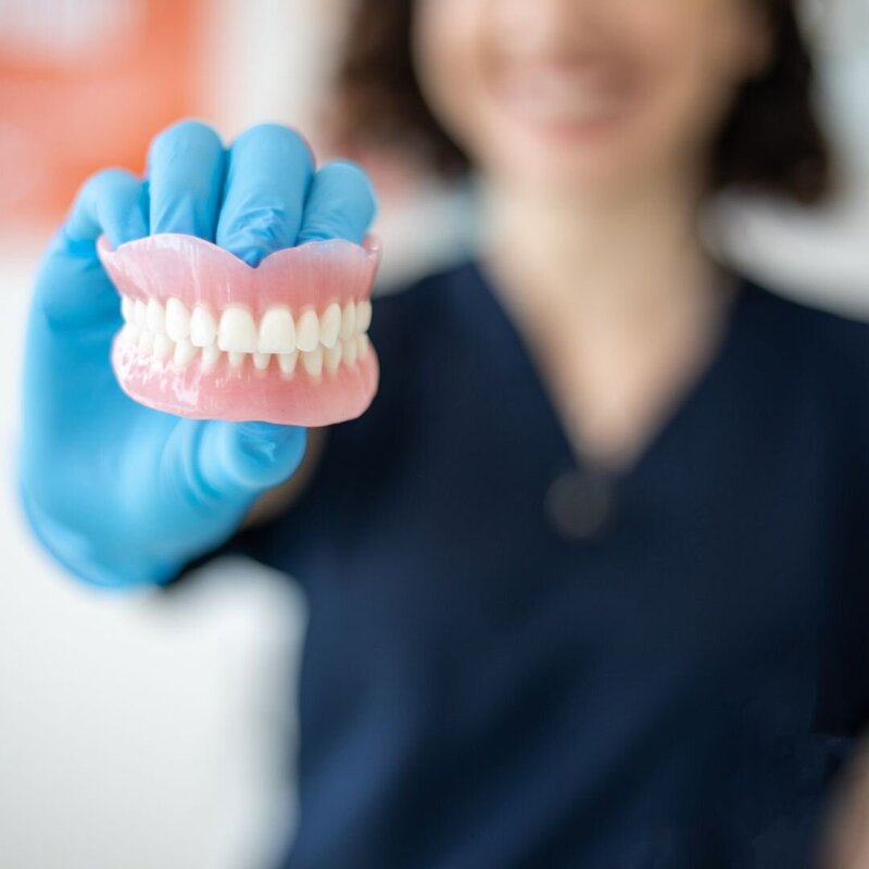 A prosthodontist at Peak Prosthodontics holding a prosthesis, reminds patients to contact the office if they notice bleeding, swelling, looseness, or persistent bad breath, as these may be signs of infection or other concerns with their dental prosthesis.