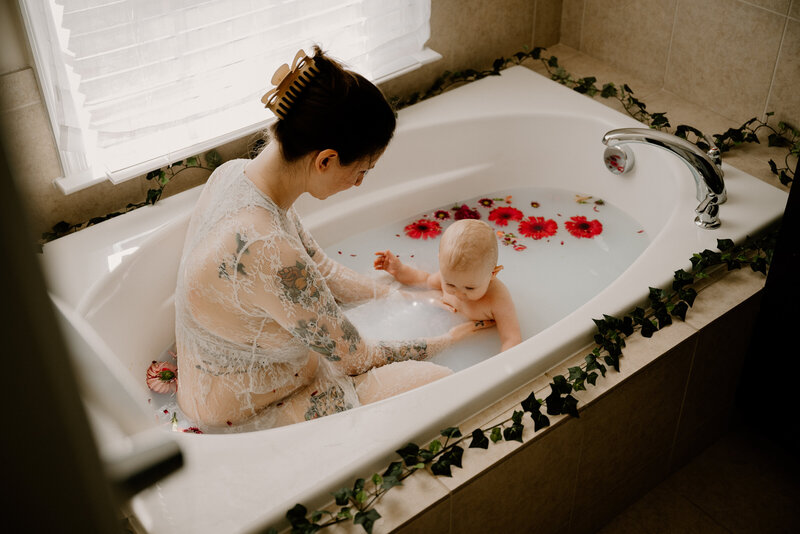 Mommy and me photo of mom in milk bath wearing white with baby girl with flowers in the water in Annapolis Maryland.
