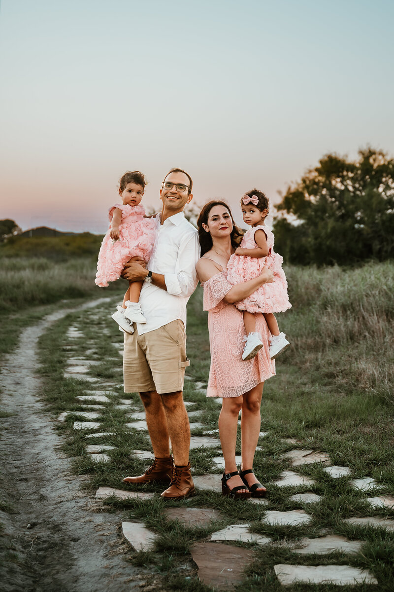 Mom and dad holding their daughters as they take family portraits during sunset in Corpus Christi, Texas.