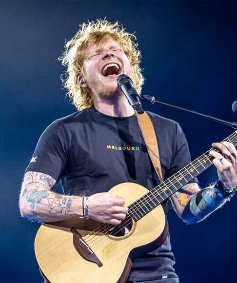 Ed Sheeran sings with energy while playing acoustic guitar live on stage wearing Melbourne shirt