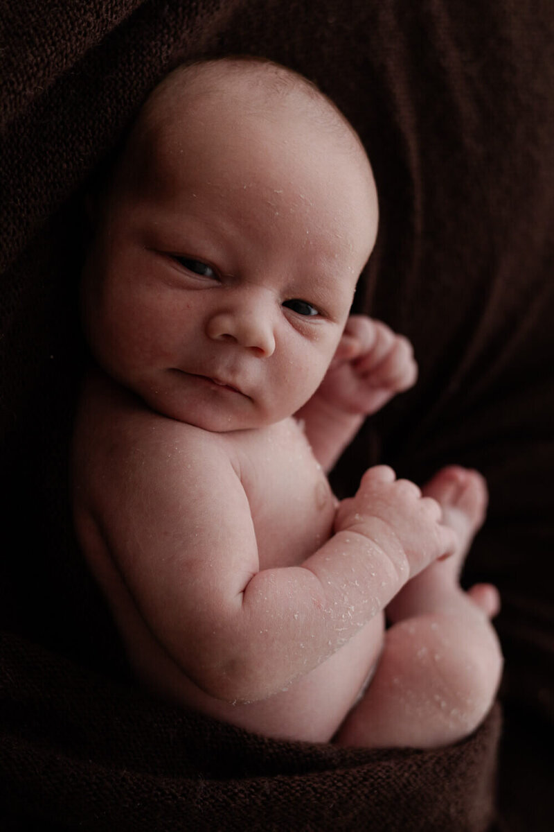 Baby in een ontspannen pose, gefotografeerd tegen een zachte bruine achtergrond. Professionele newborn shoot
