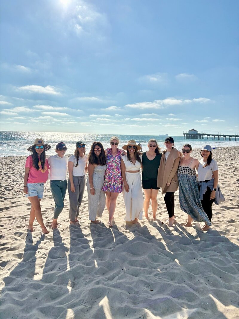 Group of women in colorful swimsuits raising arms on the beach, symbolizing The CEO Besties community