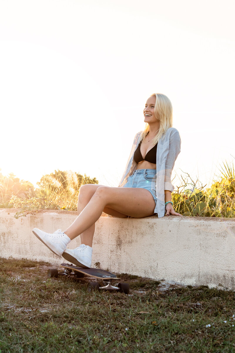 Model sits on seawall posing with skateboard on Lido Beach, FL