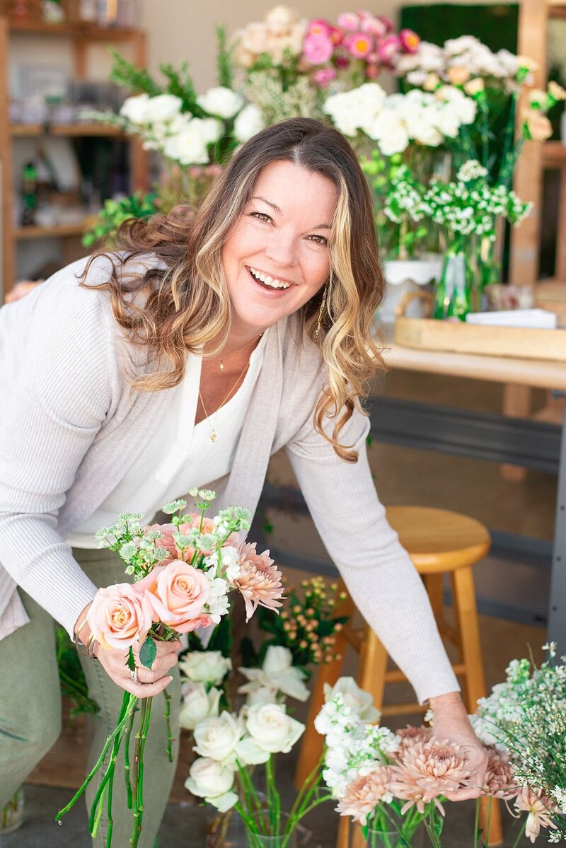 Florist leaning down to pick up flowers for a bouquet while smiling at the camera