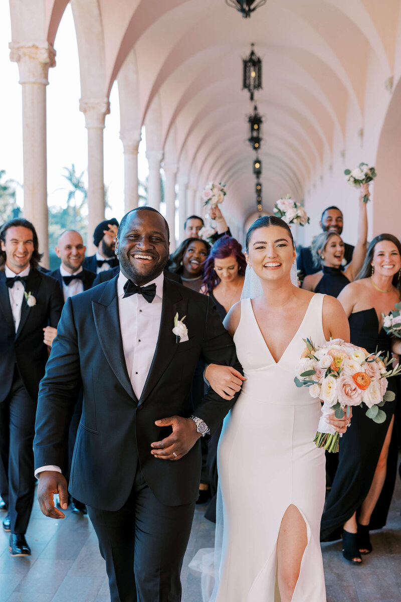 Bride and groom linking arms with their wedding party in the background