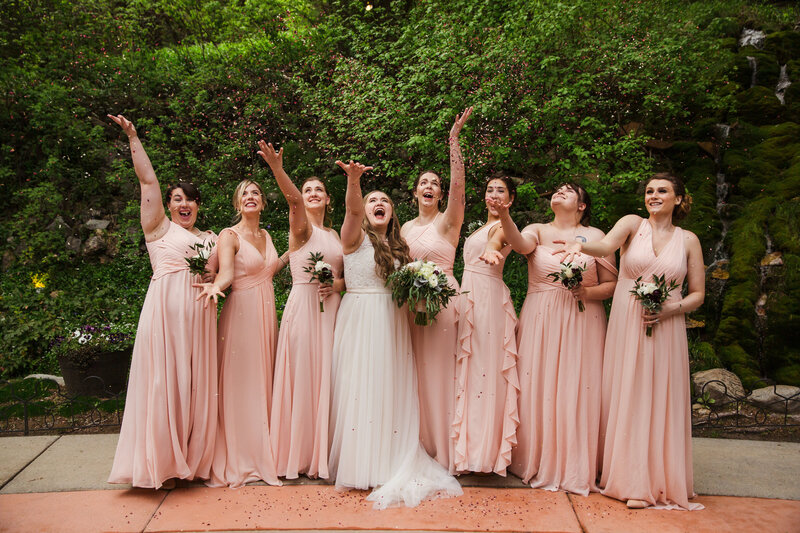 bride celebrating with bridesmaids wearing pink dresses and holding floral bouquets
