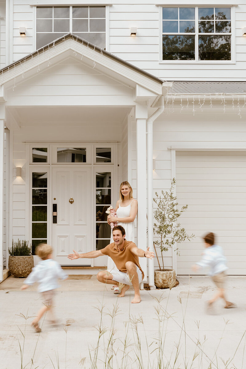 Family enjoying time together while Mum holds a newborn baby and Dad runs around with the two boys having fun - Brisbane Newborn Photographer
