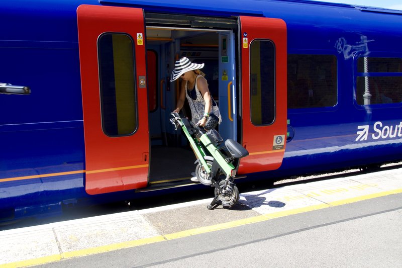Lady loads Folded up Green Go-Bike M2 on to train
