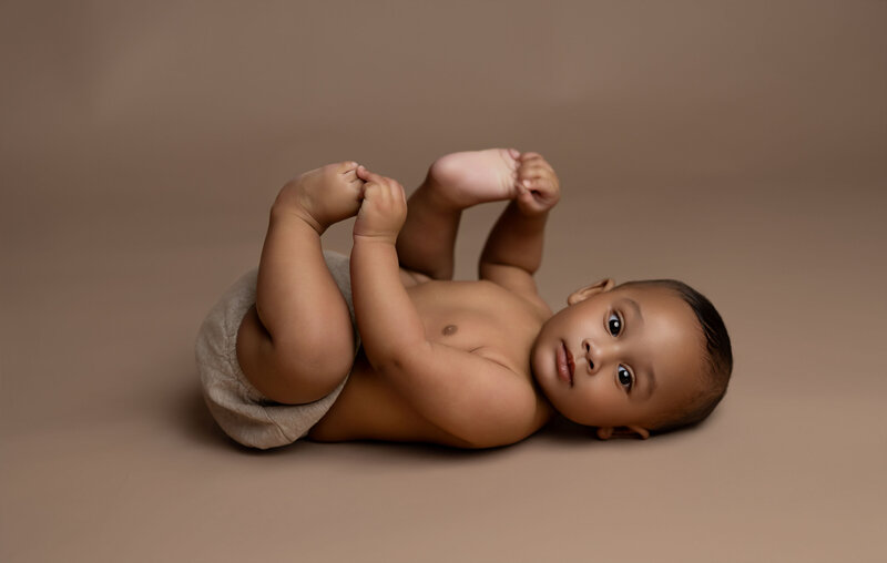 Milestone photo of baby grabbing toes. Milestone photo taken by Jenni Nikki at Atlanta Baby Photo Studio.