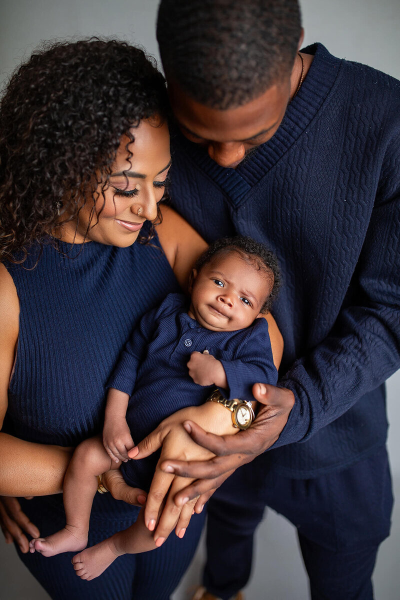 Dark haired mom and dad smiling and looking at baby with holding baby in studio in Tampa, FL