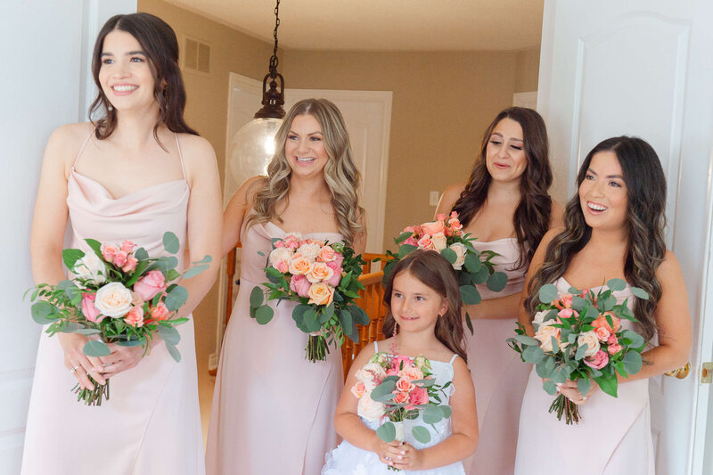 bridesmaids in pink dresses smiling as they see the bride for the first time.  Captured by Ottawa wedding photographer JEMMAN Photography