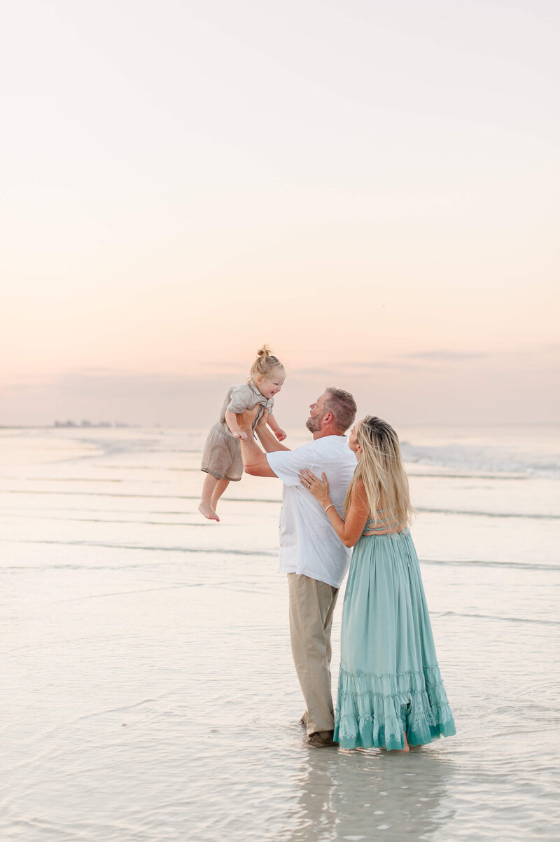 Dad stands in the water holding son in the air during family photos on Melbourne Beach, Florida