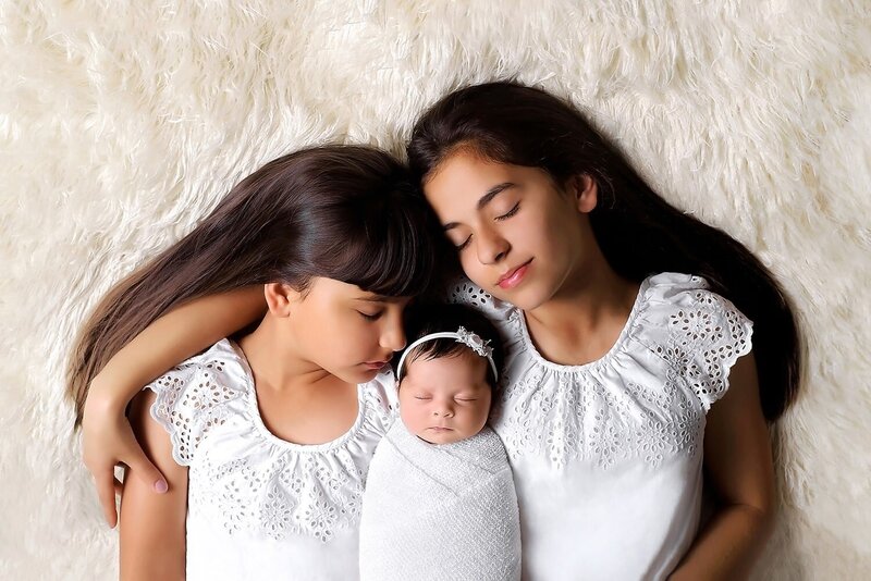 Newborn photos in Vancouver with two older sisters and 12 day newborn girl in white