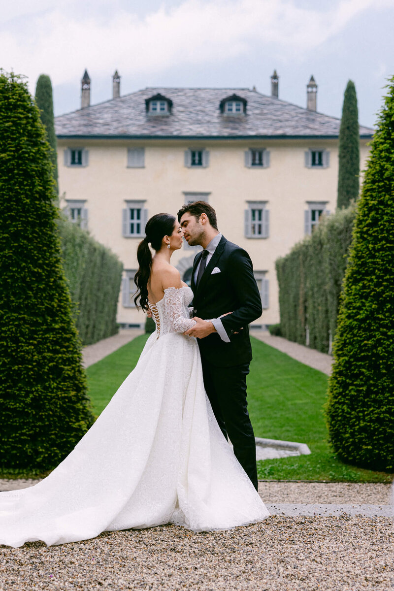 A wedding photo of a couple kissing with villa balbiano in the background at lake como in italy