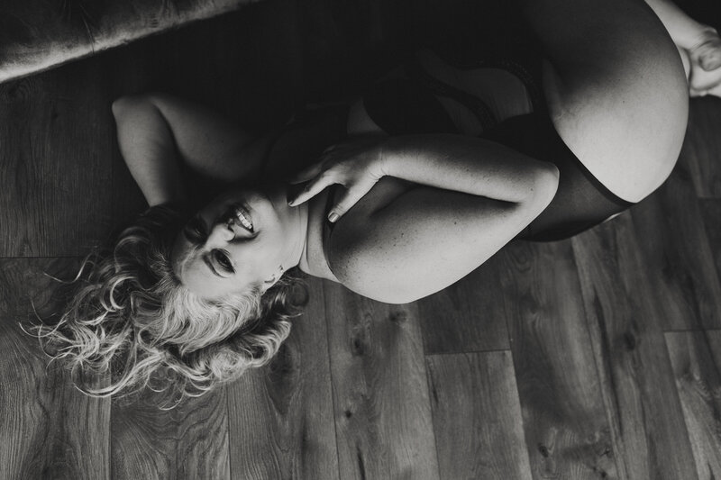 Woman laughing and lying on wood floor during black and white boudoir shoot in Gainesville, Florida studio
