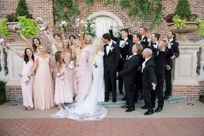 Bride and groom kissing while bridal party cheers around them