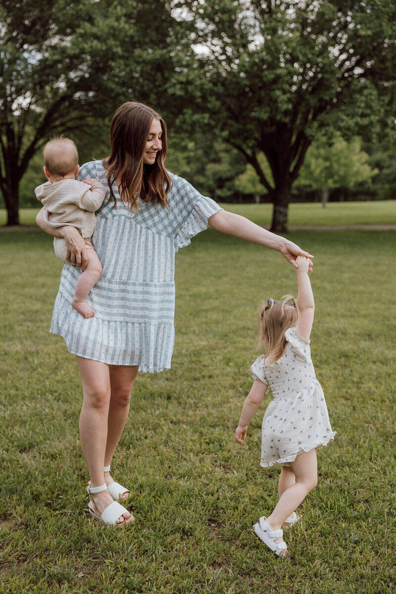 Mother holding baby son while twirling toddler daughter's hand while dancing. 