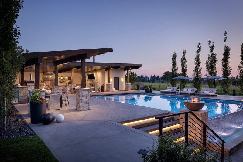 Outdoor backyard and pool with fire bowls and pergola, light features and pool loungers and black and white umbrellas. 