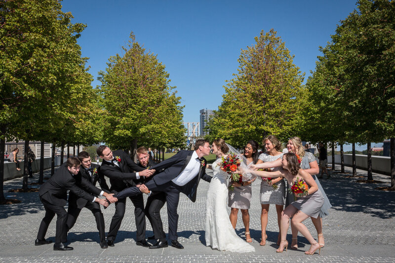 Bridesmaids and groomsmen holding back a bride and groom as they try to kiss.