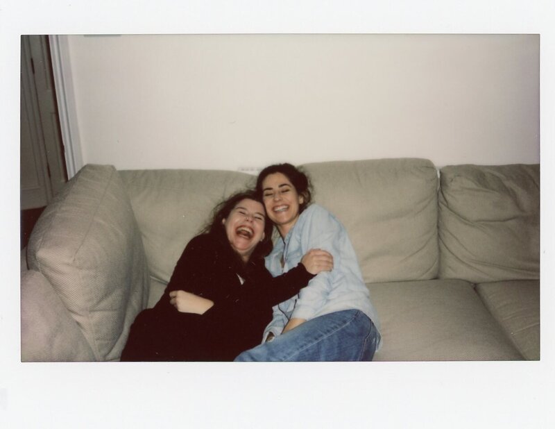 Polaroid of two women laughing and cuddling on tan couch