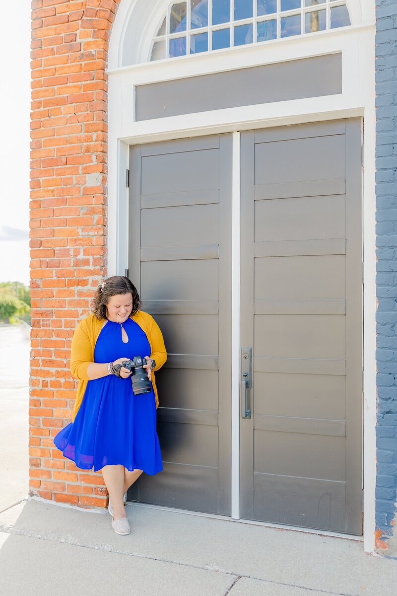 April Fox holding her camera leaning against a wall in Port Huron.