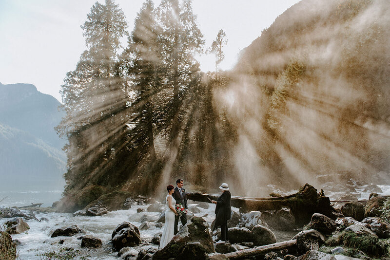 Sun streaming through the trees and mist from the waterfall during this couples elopement