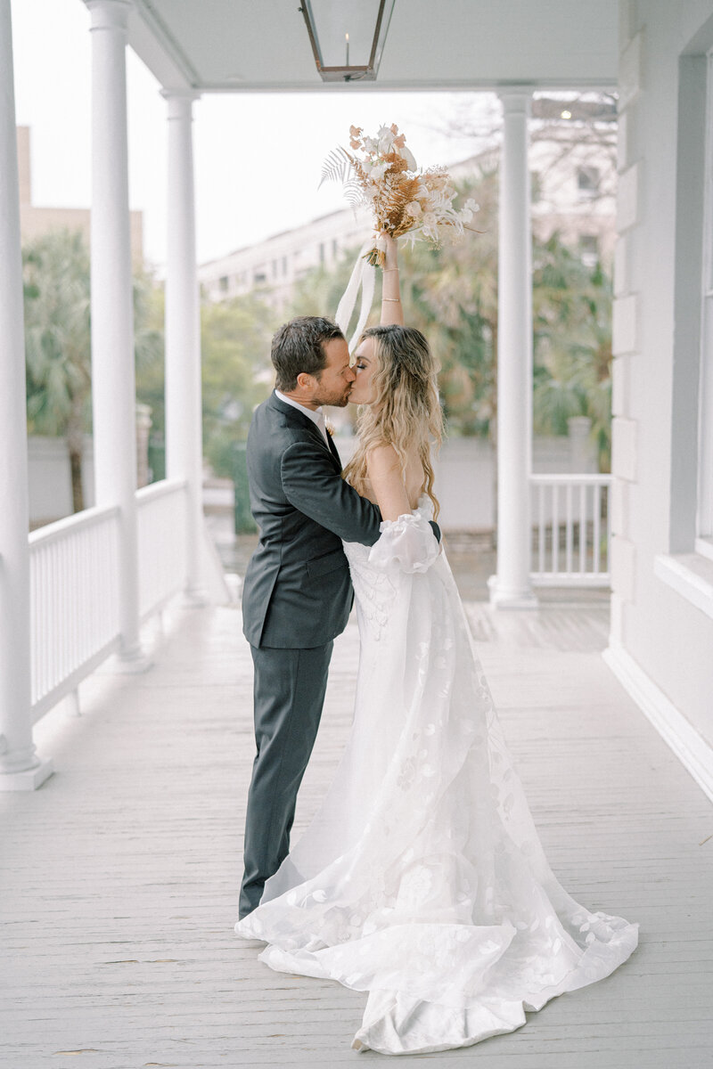 a bride and groom kissing on a porch at the gadsden house in charleston