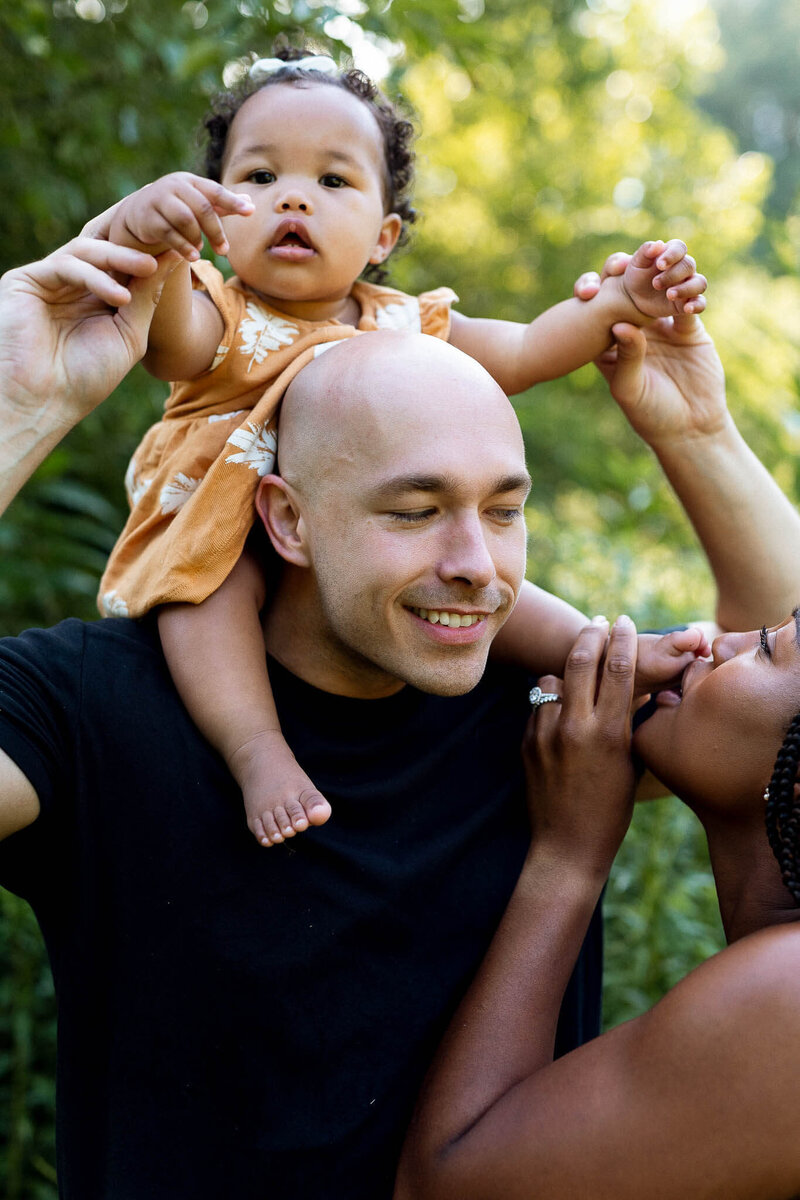 Cute baby riding on dad's shoulders while mom kisses baby's toes.
